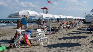 En strand med rækker af hvide parasoller og liggestole, et livredder tårn og en sandstrand.