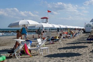 Ein Strand mit Reihen weißer Sonnenschirme und Liegestühle, einem Rettungsturm und einem sandigen Ufer.