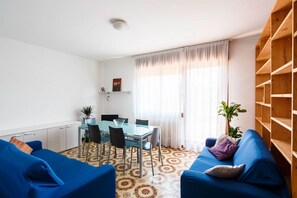 Ein Zimmer mit Esstisch, Stühlen, einem blauen Sofa, einem gestreiften Boden und einem Holzbücherregal.