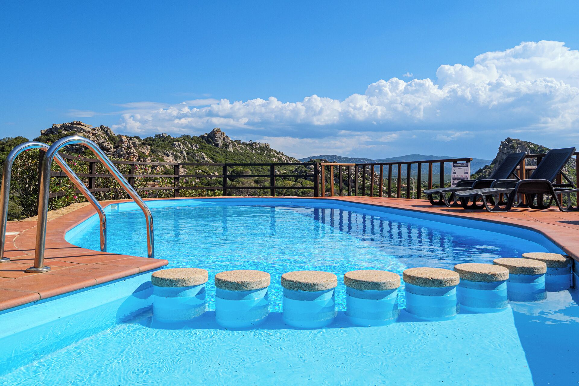 Ein Schwimmbecken mit Holzdeck, Metallgeländern und Liegestühlen.