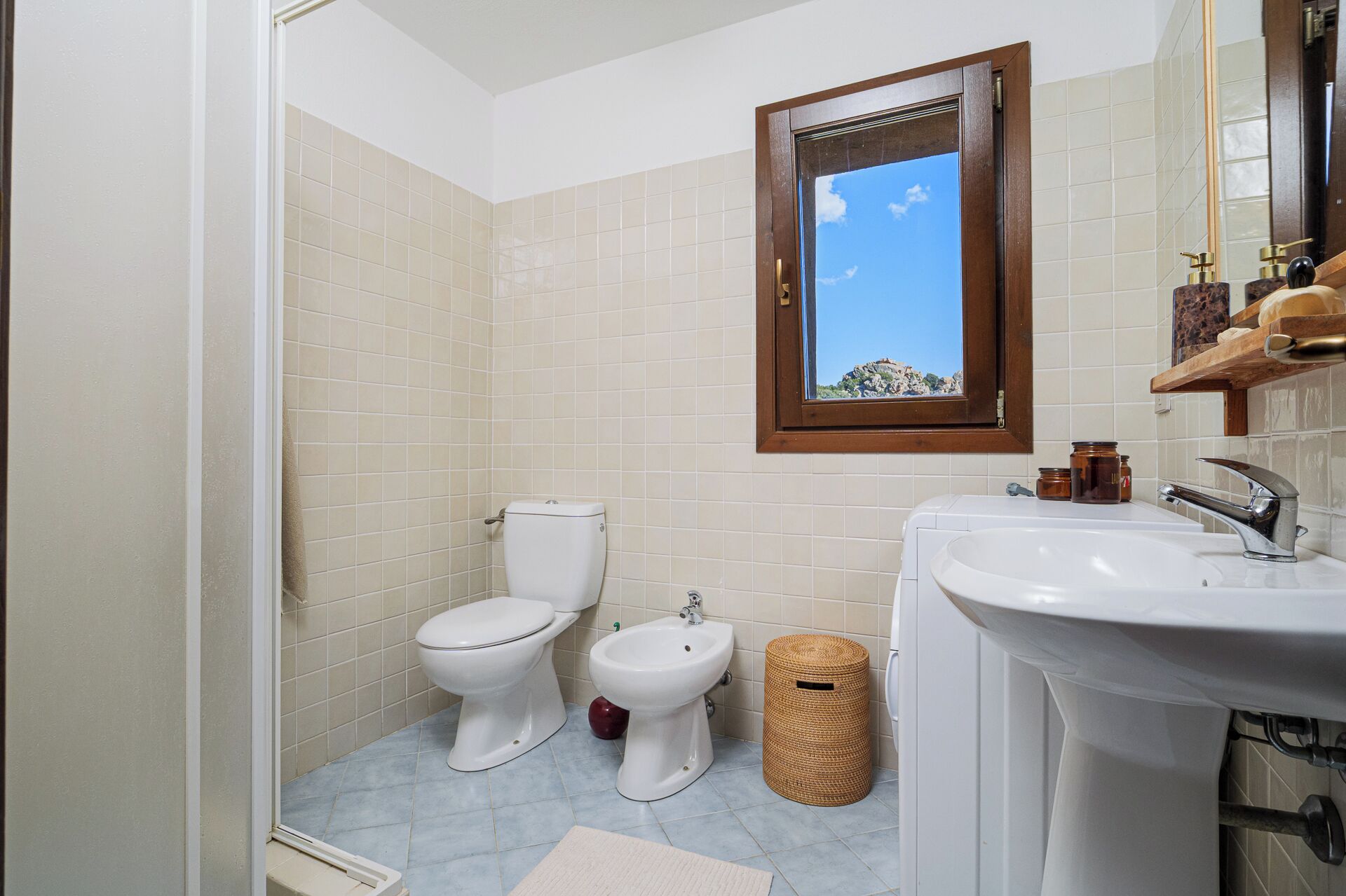 Une salle de bain équipée de toilettes, d’un bidet, d’un lavabo et d’une fenêtre donnant sur un paysage agréable.