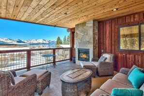 A covered outdoor seating area with wicker furniture, a stone fireplace, and a view of snow-capped mountains. - Lakeview Grand Lodge | Rooftop Deck | Theater (South Lake Tahoe)
