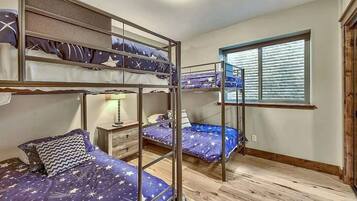 Une chambre de dortoir avec des lits superposés, une fenêtre avec des stores, une table de chevet avec une lampe et un plancher en bois.