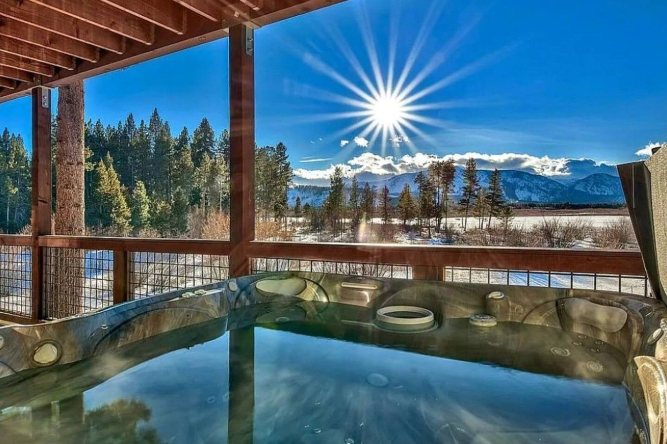 Un bain à remous offrant une vue dégagée sur un paysage montagneux enneigé et sur un soleil éclatant.