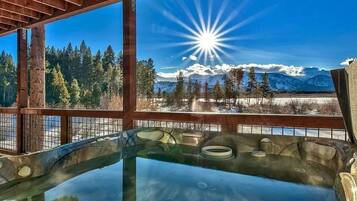 Un bain à remous offrant une vue dégagée sur un paysage montagneux enneigé et sur un soleil éclatant.