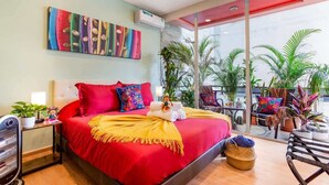 Ein modernes Hotelzimmer mit einem großen Bett, Blick ins Freie und einem farbenfrohen, abstrakten Gemälde an der Wand.
