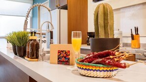 Eine Küchenarbeitsplatte mit einem Kaktus, einem Glas Orangensaft, einem Korb getrockneter Chilis und einer Kaffeemaschine.