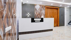 Zona de recepción con suelo de mármol, mostrador de recepción que dice 'PALETTE', un ventilador de pared y una puerta de madera.
