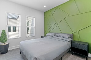Un dormitorio moderno con cama, mesitas de noche, una pared de acento verde y dos ventanas con persianas.