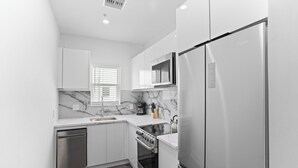 A modern kitchen with white cabinetry, a built-in oven, a stainless steel refrigerator, and a marble backsplash. - Hyde Park 1/1 private residence 12 (Tampa)