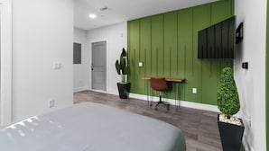 Una camera da letto moderna con un letto, una scrivania, una sedia, una pianta in vaso e una TV a parete.