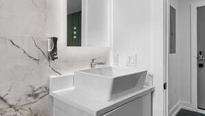 Un bagno moderno con un lavandino bianco, uno specchio e una parete in marmo.