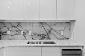 Et moderne køkken med hvide skabe, et marmor backsplash, en stålvask og en indbygget opvaskemaskine.