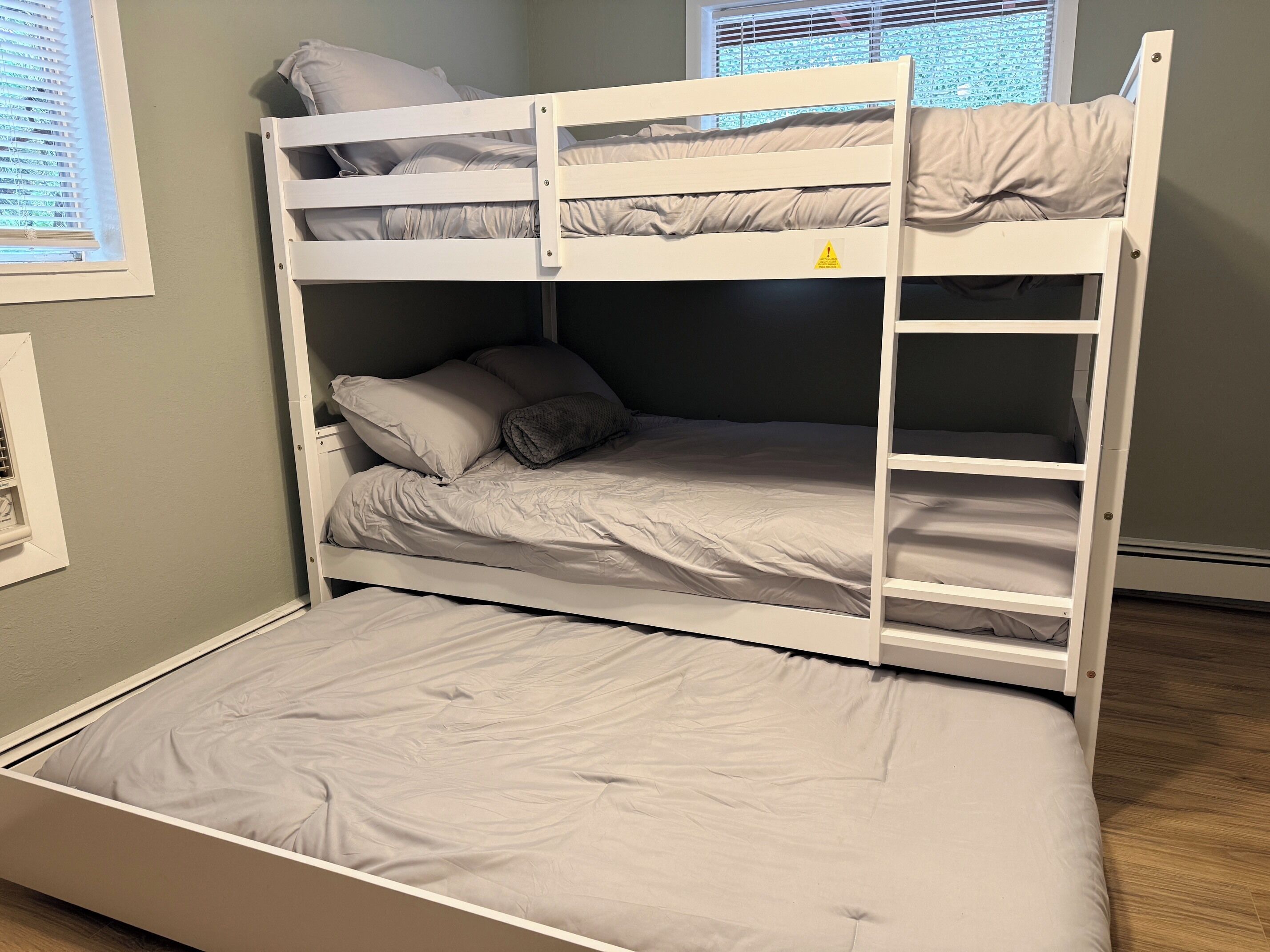 A bunk bed with a ladder, a window with blinds, and a wall-mounted heater.