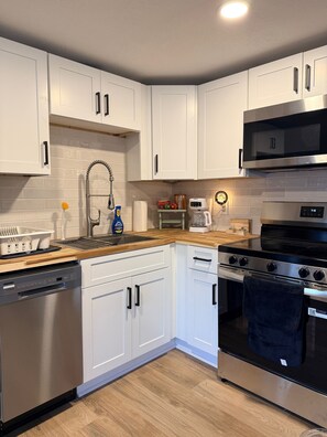 A modern kitchen with white cabinets, stainless steel appliances, and a wooden countertop. - Pleasant Valley RV (Howard)