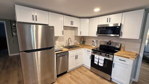 A modern kitchen with white cabinets, stainless steel appliances, and a wooden countertop.