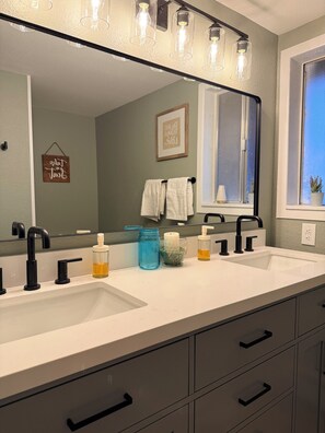 A bathroom with two sinks, black faucets, a large mirror, and a window with a view. - Pleasant Valley RV (Howard)