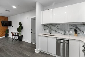 Een moderne keuken met witte kastjes, een marmeren spatwand en een RVS vaatwasser.