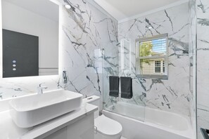 Un bagno moderno con un ampio lavandino bianco, un WC e una vasca da bagno vetrata.