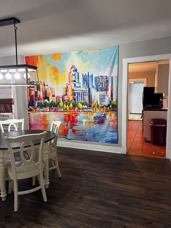 A dining area with a table and chairs, a kitchen with cabinets and a stove, and a colorful cityscape painting on the wall.
