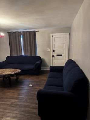 A living room with two dark blue sofas, a round wooden coffee table, and a white door with a keypad lock.