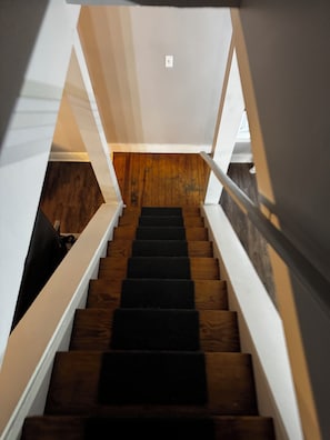 A staircase with wooden steps and white railings, leading to a landing with a light switch.