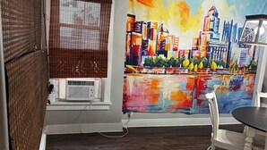 A room with a cityscape painting, a piano, a dining table with chairs, and a window with blinds. - 3-bedroom house in Southside Flats neighborhood of Pittsburgh. (Pittsburgh)