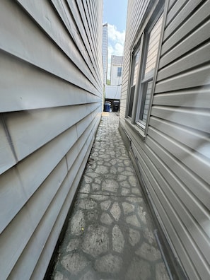A narrow pathway between buildings with a stone-patterned floor and metal siding.