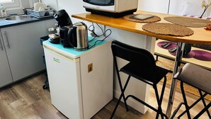 Una cocina compacta con refrigerador, microondas, hervidor y cafetera sobre una pequeña encimera.