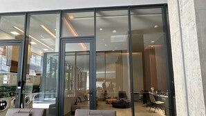 A modern indoor lounge area with two lounge chairs and a round ottoman, a glass door leading to a dining area, and a visible laundry facility in the background. - Millenium Luxury Cozy Studio in Vila Ol Mpia (São Paulo)