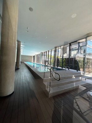 Ein moderner, überdachter Pool mit Glaswänden, Holzterrasse und Blick auf die umliegende Landschaft.