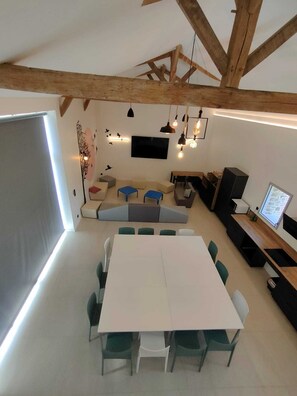 Un intérieur moderne avec une table blanche, des chaises vertes, un canapé et un téléviseur fixé au mur.