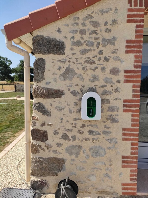 A stone wall with a green electrical outlet and a metal manhole cover.