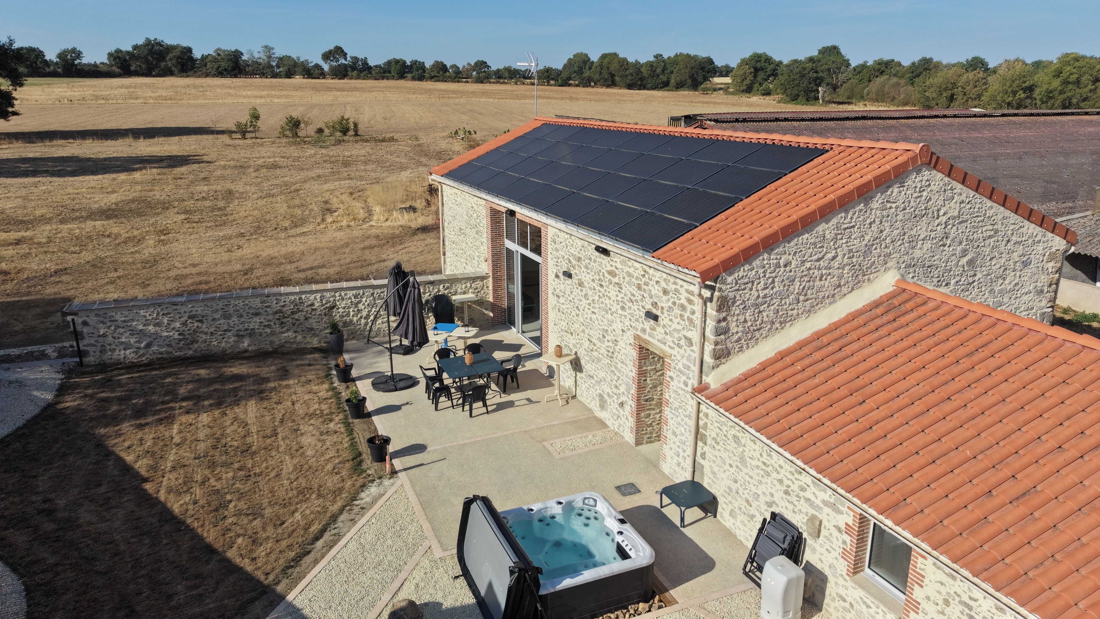 Un bâtiment en pierre surmonté d’un toit équipé de panneaux solaires, une terrasse avec des meubles d’extérieur et un jacuzzi.