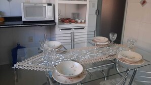 A dining area with a glass table set for four, a white microwave, and shelves with glassware and dishes. - chacara temporada manu tobar brotas sp (Brotas)