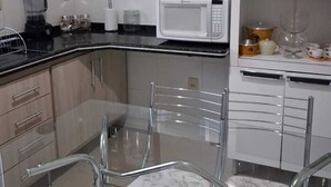 A modern kitchen with a glass dining table, white cabinets, and a microwave. - chacara temporada manu tobar brotas sp (Brotas)