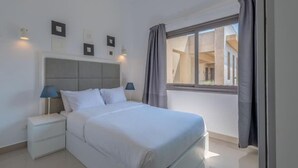 A bedroom with a bed, nightstands, a window with curtains, and wall-mounted lights. - Gcribs apartment pool view (Hurghada)