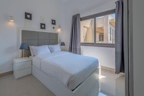 Ein Schlafzimmer mit Bett, Nachttischen, einem Fenster mit Vorhängen und Wandleuchten.