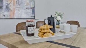 Uma bandeja de café da manhã com croissants e geleia, uma prensa francesa e xícaras brancas sobre uma mesa de madeira.