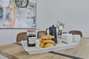 A breakfast tray with croissants and jam, a French press, and white cups on a wooden table. - Modern vacation home on the canal with a saltwater pool and private dock in the yacht club area (Cape Coral)