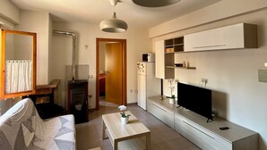A modern living room with a sofa, a coffee table, a TV, and a kitchen area with cabinets and a microwave. - Maiella Experience - Downtown Apartment, Nestled in the Maiella Mountains (Campo di Giove)