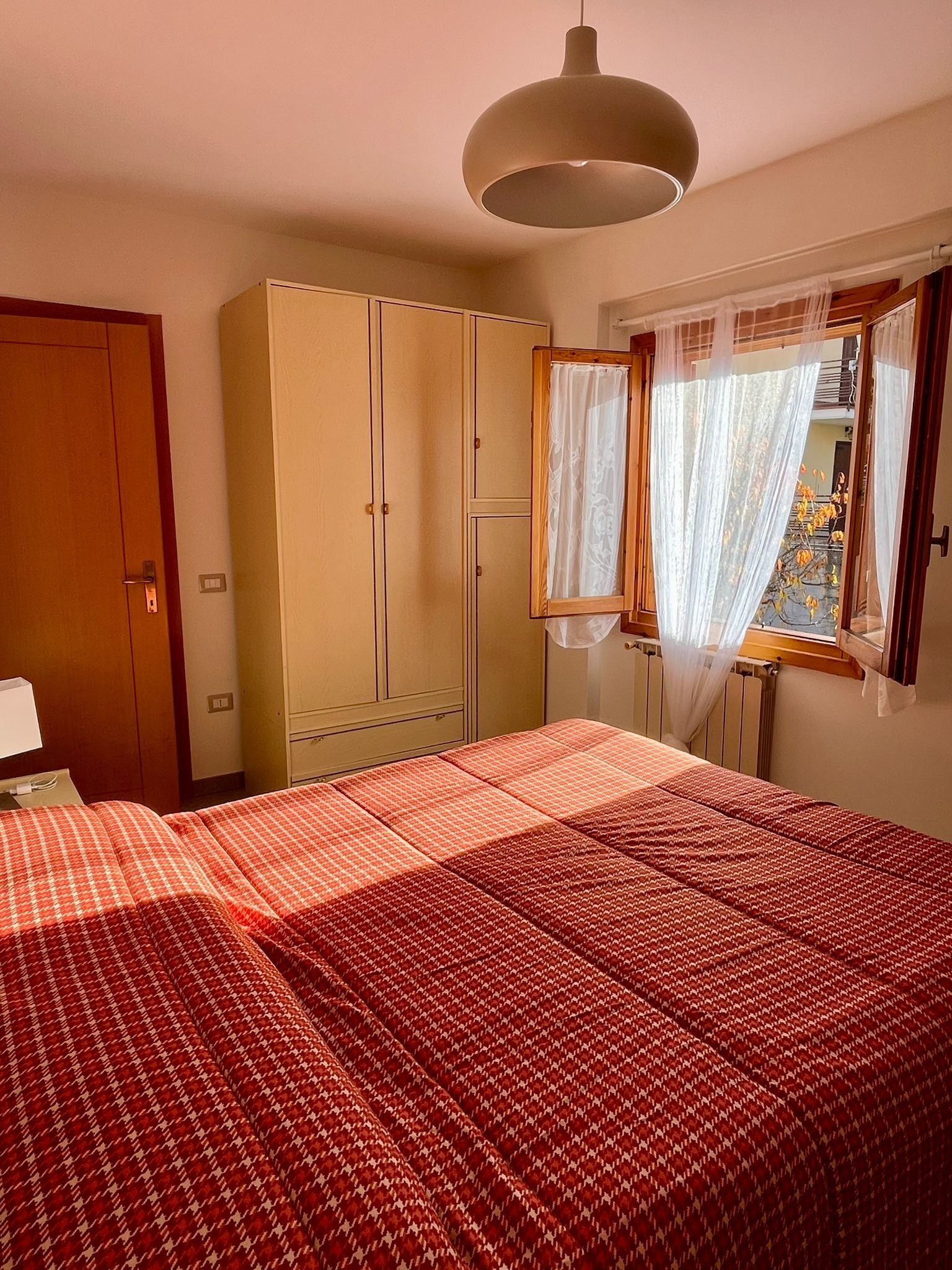 Un dormitorio con cama, armario y ventana con cortinas.