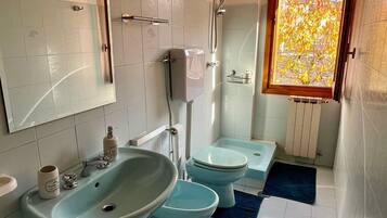 A bathroom with two sinks, a toilet, a shower, and a window with a view of trees.