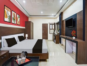 A hotel room with a bed, bedside table, TV, and artwork on the wall. - Deluxe Prayagraj Central Shantila Inn (Prayagraj)