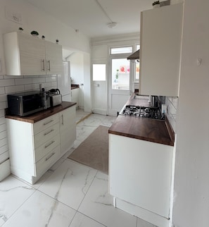 A modern kitchen with white cabinetry, a gas stove, a microwave, and a coffee maker.