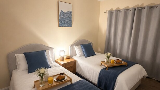 A hotel room with two beds, a painting on the wall, a window with curtains, and a tray with breakfast items.