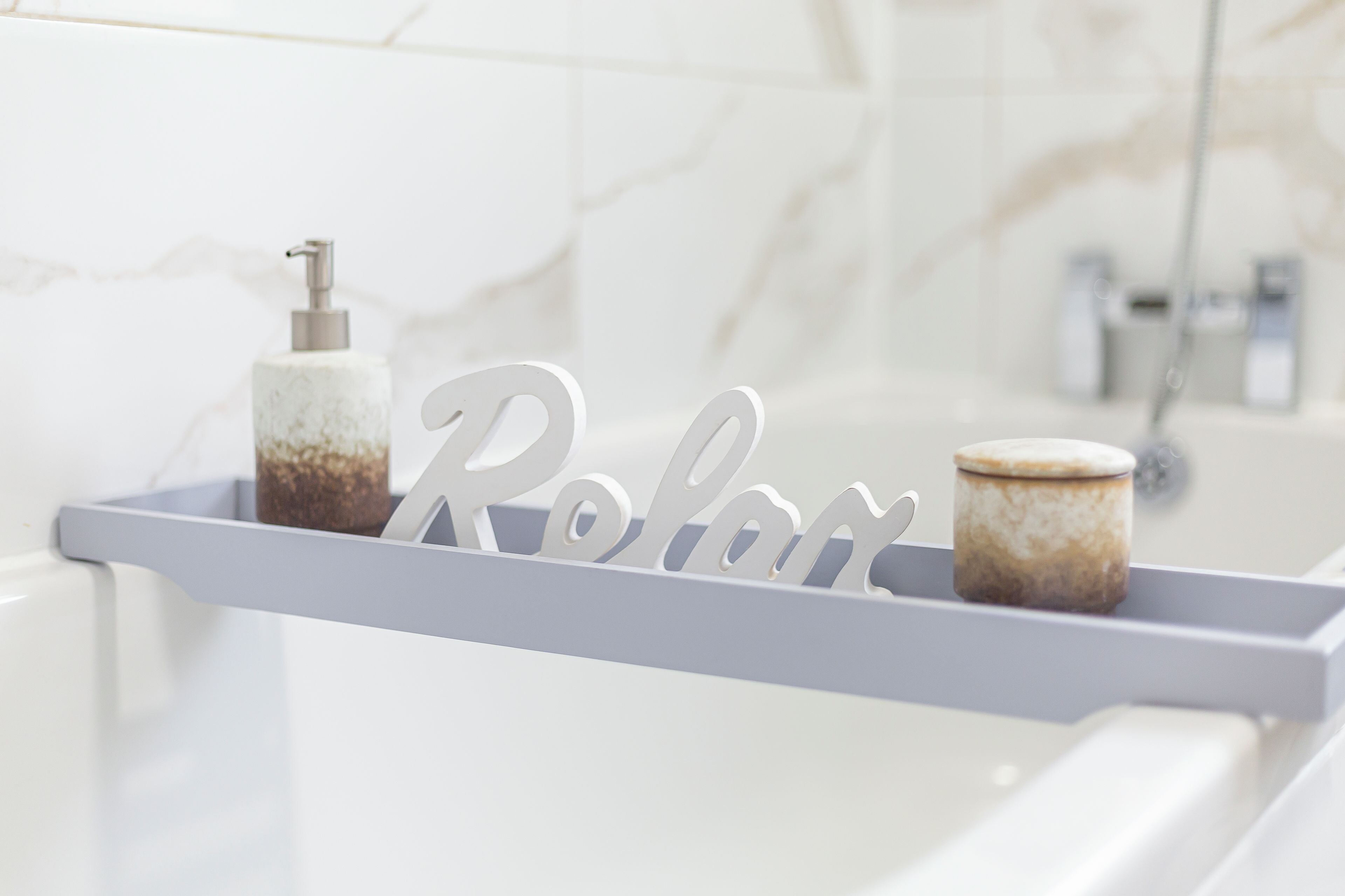 A bathroom with a marble wall, a white shelf with a soap dispenser and a candle, and a shower area.