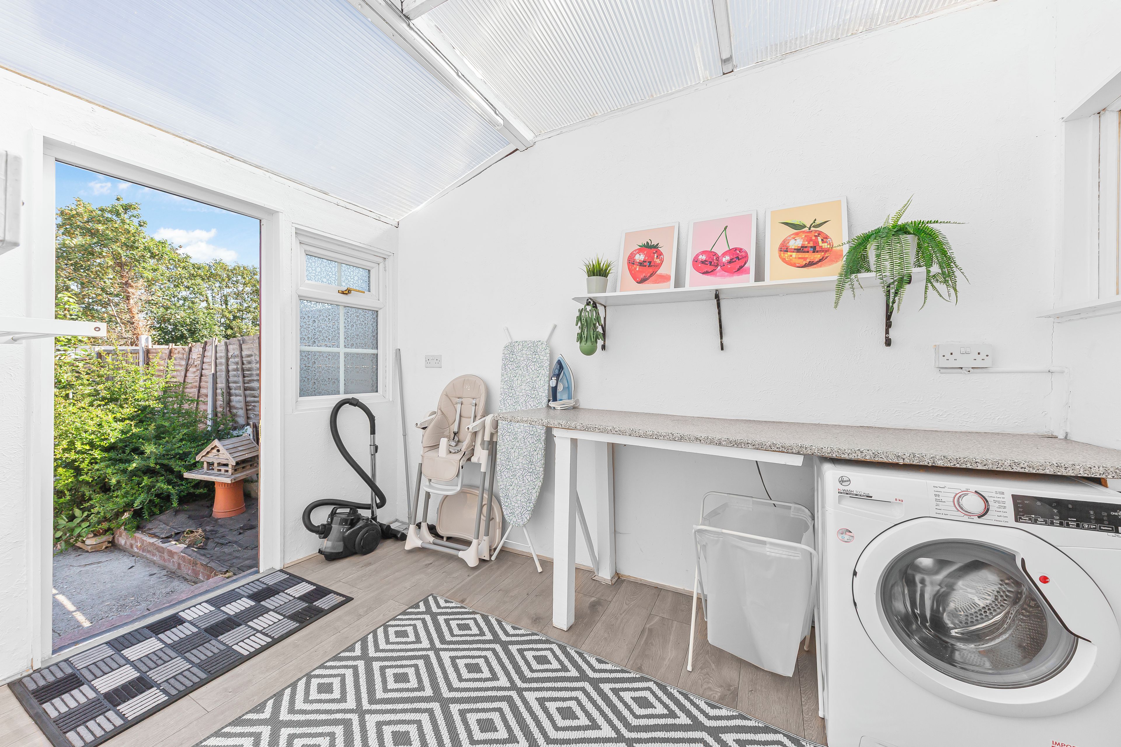 A compact laundry room with a washing machine, a vacuum cleaner, and a small ironing station.