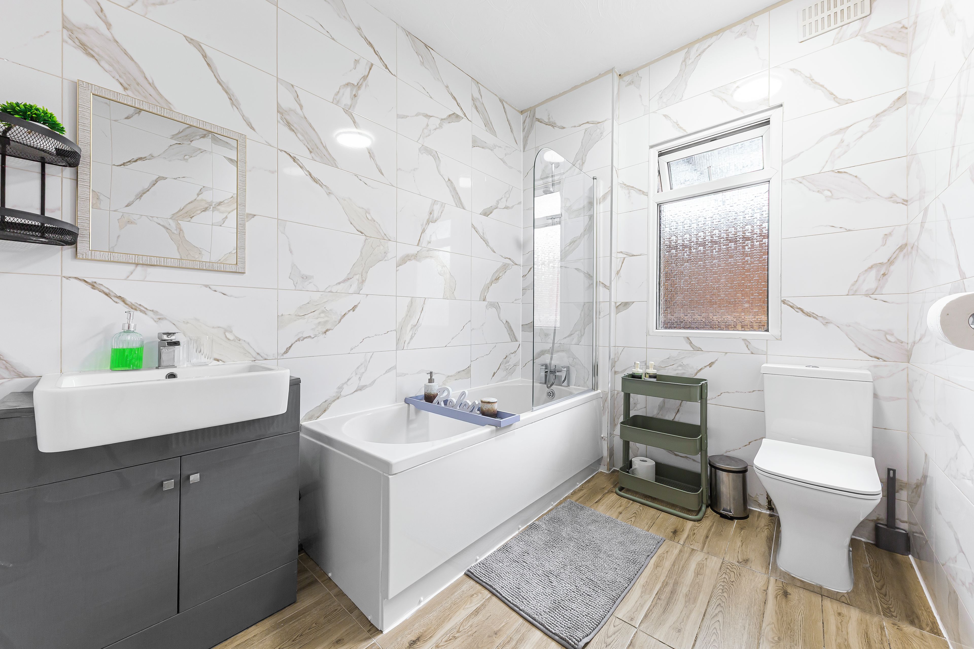 A modern bathroom with a marble wall, a bathtub, a toilet, and a sink.