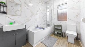 A modern bathroom with a marble wall, a bathtub, a toilet, and a sink. - Modern 4BR Home|Sleep 7|Free Parking|Self check in (Southend-on-Sea)